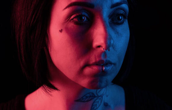 ritratto in primo piano di una donna illuminata da una luce rossa e da una luce blu su fondo nero