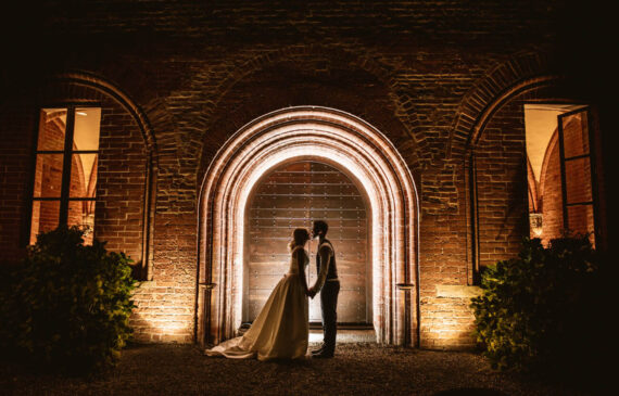 due sposi si baciano davanti ad un portico illuminato di notte presso il Principato di Lucedio a Trino vercellese