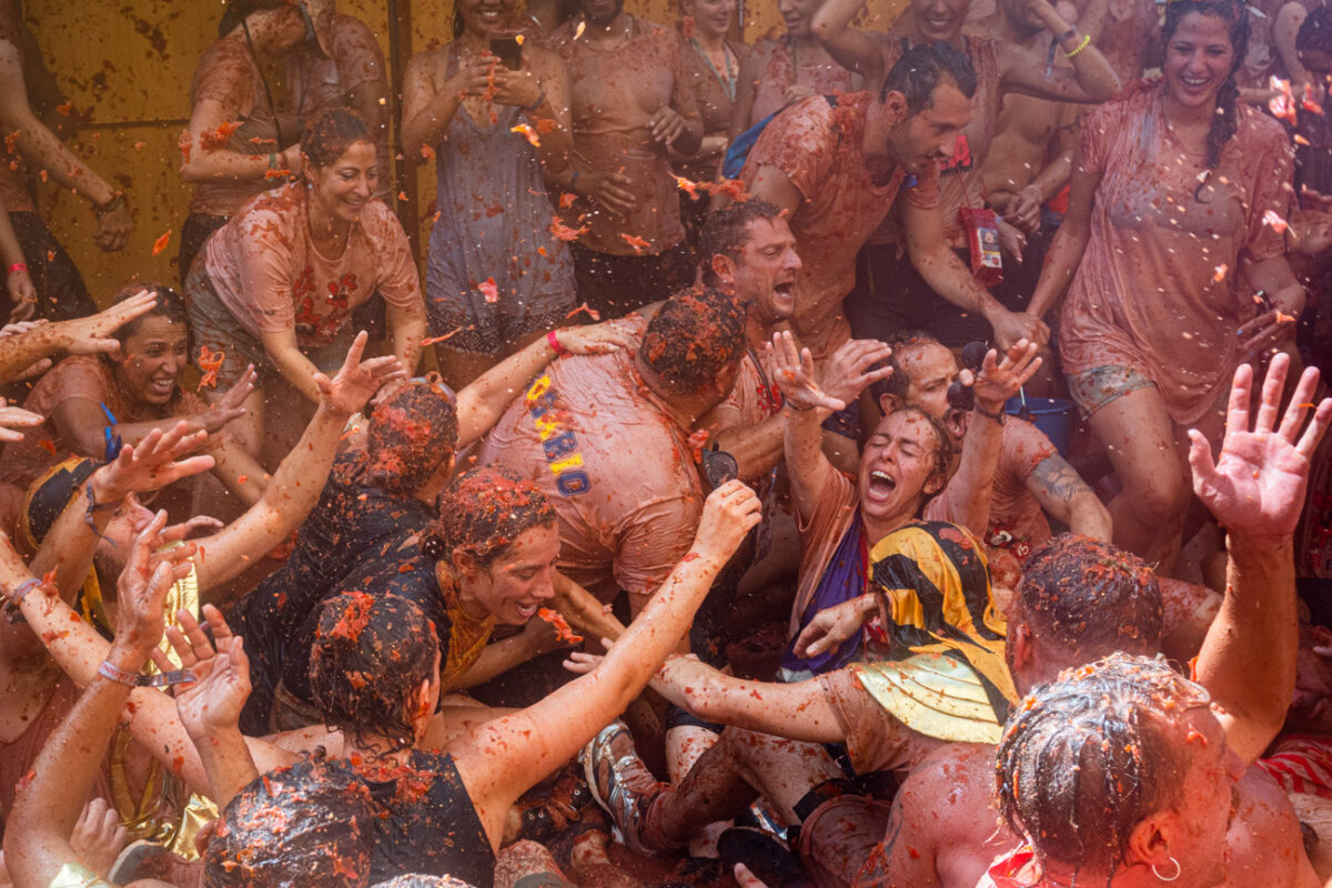 Uomini e donne pieni di salsa di pomodoro ridono e ballano durante il festival la tomatina a Buñol