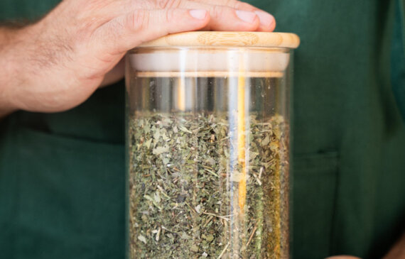 Un uomo con il grembiule recante il logo Ricola tiene tra le mani un barattolo con delle erbe