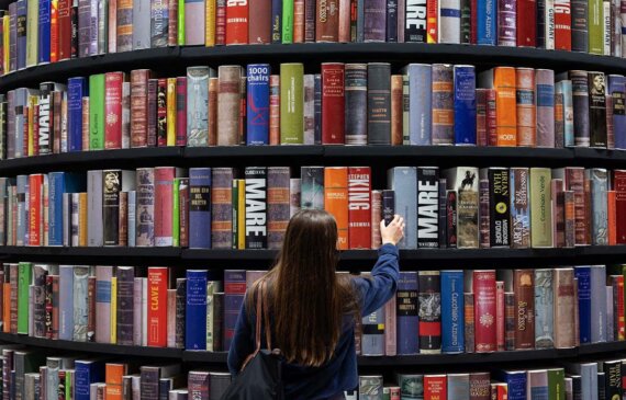 Una giovane ragazza prende un libro da una parete piena di libri