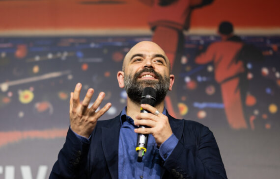 Roberto Saviano sorride mentre parla al microfono