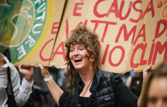 una ragazza sorride mentre tiene un cartello di protesta control il cambiamento climatico a Torino