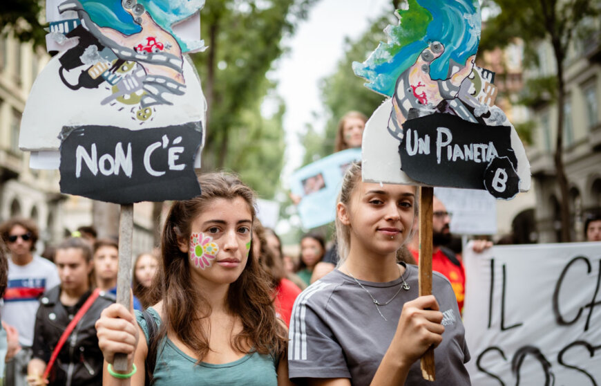 Due ragazze posano mentre portano cartelli contro il cambiamento climatico durante una manifestazione