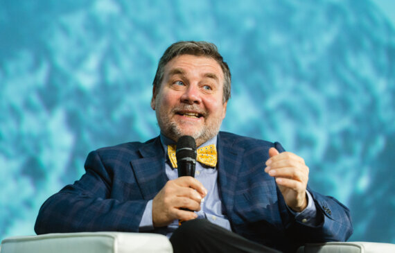 Il meteorologo Luca mercalli parla al microfono seduto su una poltrona con sullo sfondo uno schermo blu