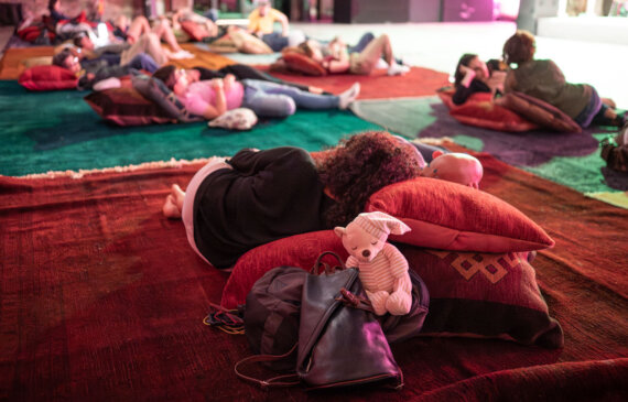 Diverse persone giacciono sdraiate durante un concerto notturno a Torino, in primo piano c'è un pupazzo raffigurante un orsetto