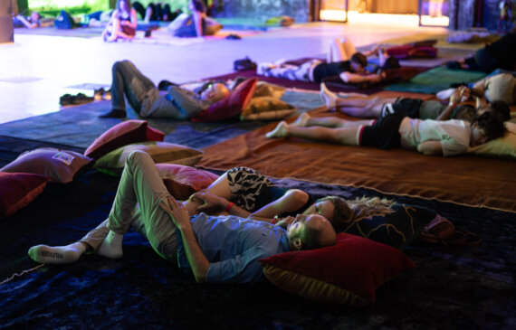 Diverse persone giacciono sdraiate su tappeti colorati durante un concerto notturno sleep concert a Torino ogr