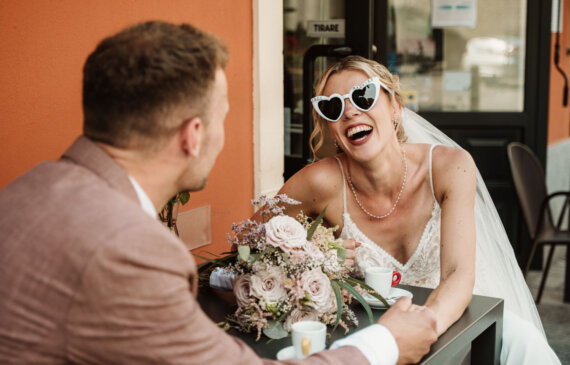Due sposi si guardano e sorridono seduti al tavolino di un bar