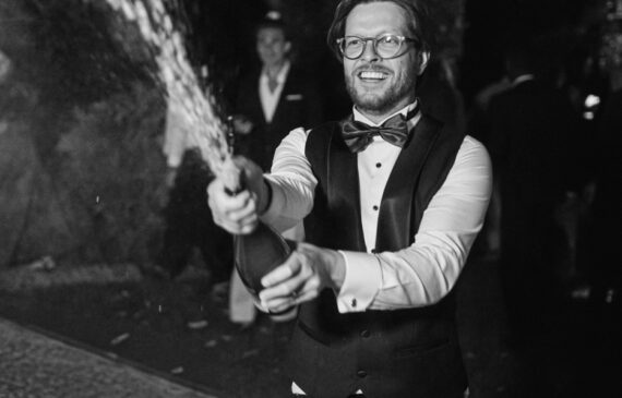 A groom popping a bottle of champagne